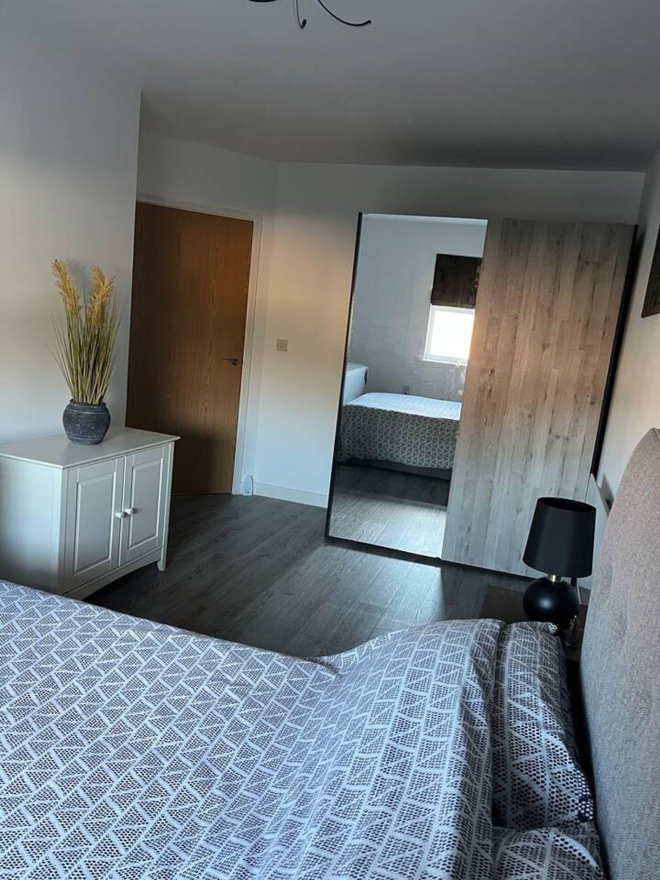 A bedroom with a bed, a dresser, a mirror, and a window.