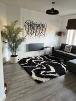 A modern living room with a large abstract painting, a potted plant, a black and white rug, and a grey sofa.