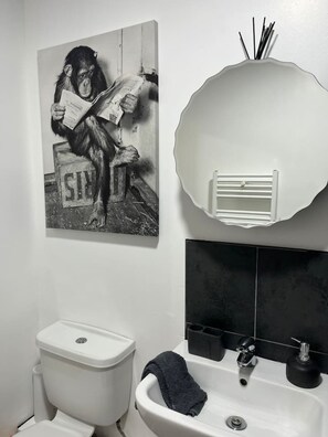 Un baño con inodoro, lavamanos y espejo, con una toalla colgada.