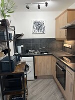 Una cocina moderna con lavadora, un lavamanos y una estufa. Hay un cuadro en la pared y una planta a la izquierda.
