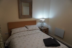 A bedroom with a bed, a nightstand, a lamp, a mirror, and a radiator. - 2B 2B Haydock Flat M6 J23 A580 Gated Parking (St Helens)