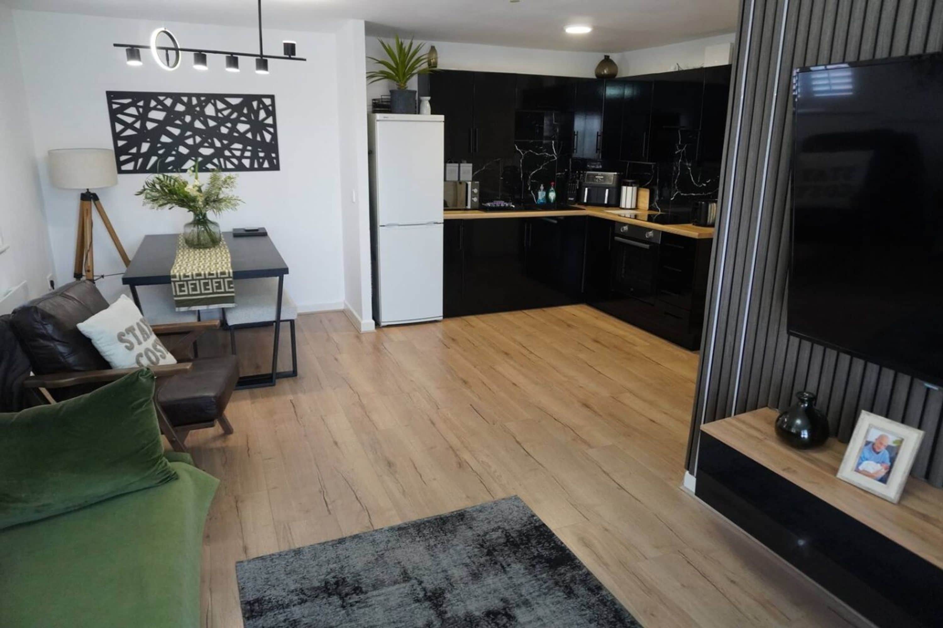 A modern living room with a sofa, a coffee table, and a dining area with a kitchen in the background.