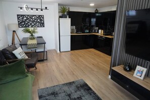 A modern living room with a sofa, a coffee table, and a dining area with a kitchen in the background. - 2B 2B Haydock Flat M6 J23 A580 Gated Parking (St Helens)