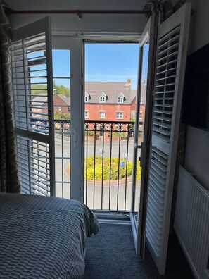 A bedroom with a bed, a window with blinds, and a view of a street and buildings. - 2B 2B Haydock Flat M6 J23 A580 Gated Parking (St Helens)