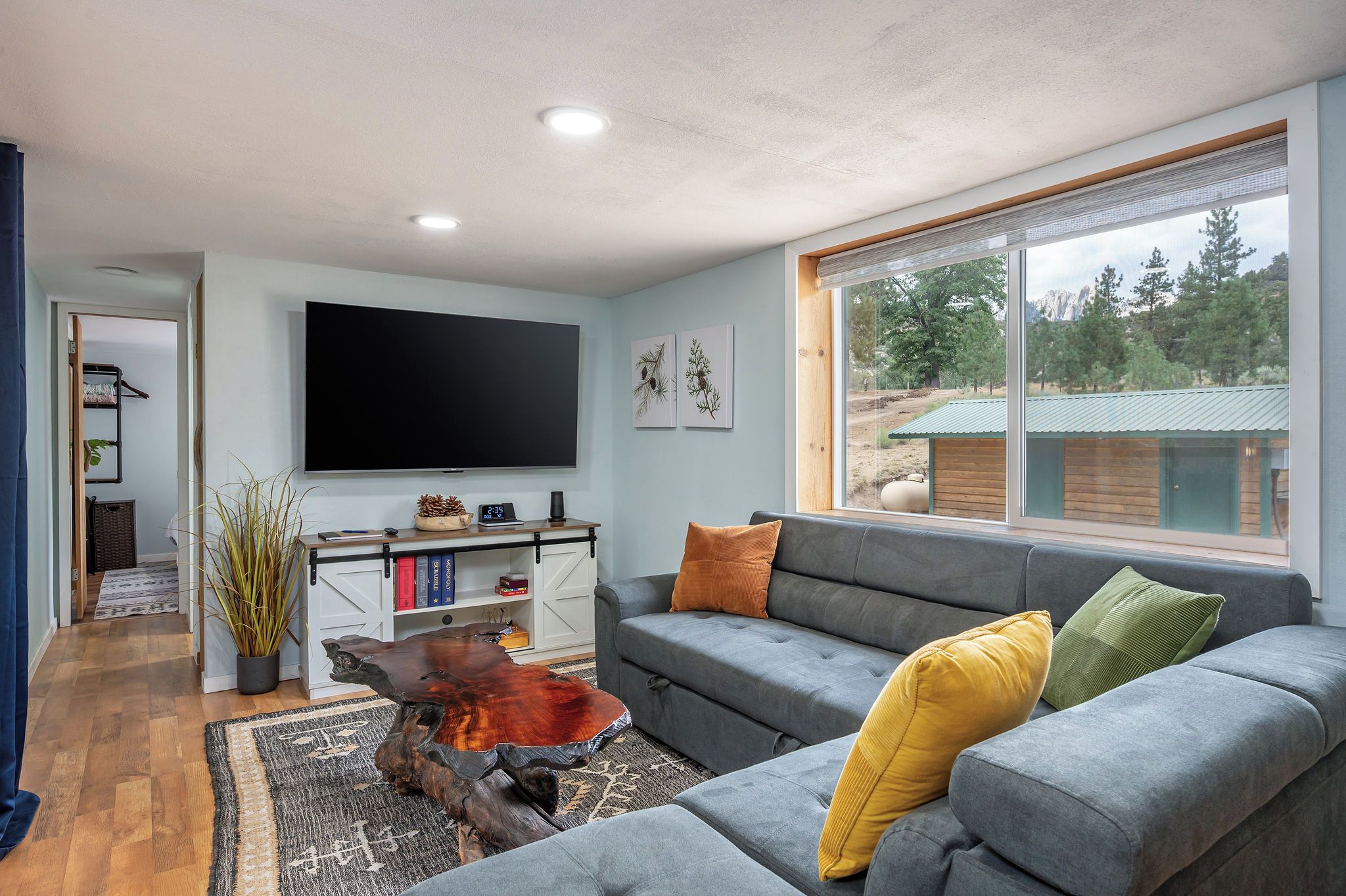 A modern living room with a grey sofa, a coffee table, and a flat-screen TV mounted on the wall.