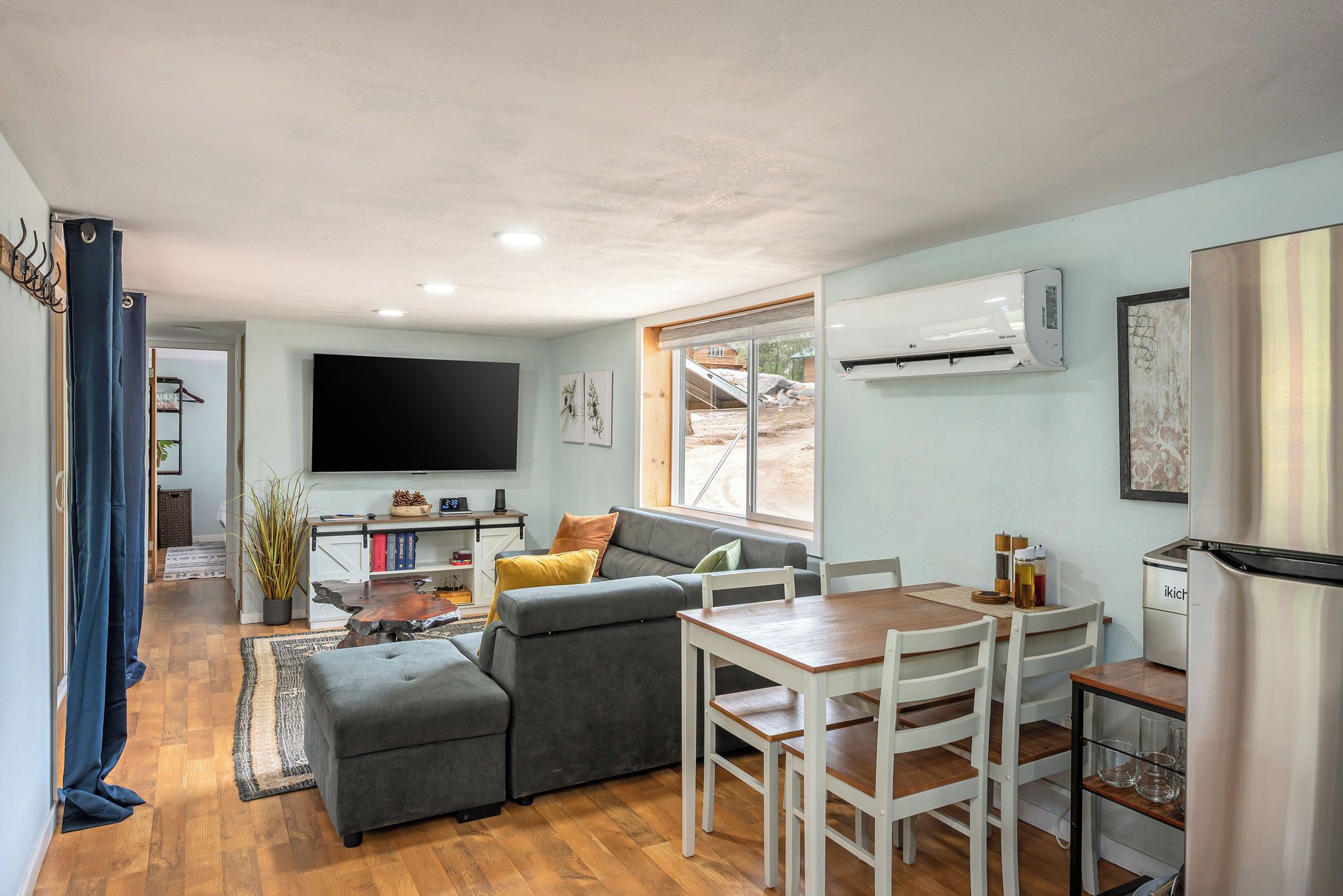 A compact living space with a sofa, a dining table, and a flat-screen TV mounted on the wall.