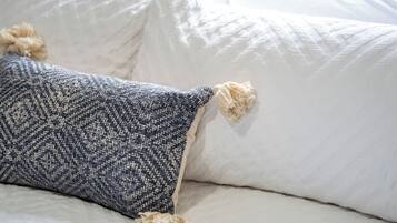 Een bed met witte lakens en een decoratief kussen met franjes.