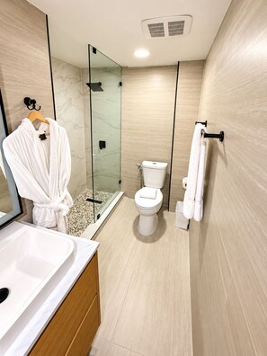 A modern bathroom with a glass shower enclosure, a white toilet, and a wooden vanity with a sink. - Deluxe King Suite, Beach Access & Prime Location (Miami Beach)