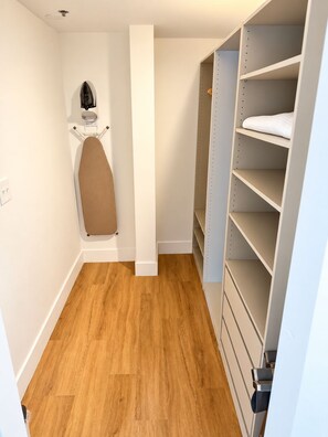 A closet with shelves and a hanging rod, a wooden floor, and a white wall. - Deluxe King Suite, Beach Access & Prime Location (Miami Beach)