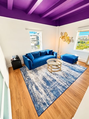 A modern living room with a blue sofa, a round coffee table, and a patterned rug. - Deluxe King Suite, Beach Access & Prime Location (Miami Beach)