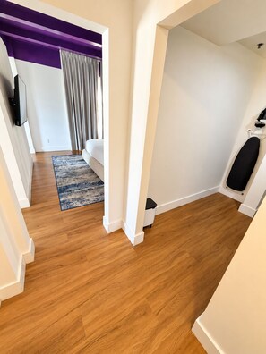 A modern hotel room with a wooden floor, a white sofa, a small rug, and a purple accent wall. - Deluxe King Suite, Beach Access & Prime Location (Miami Beach)