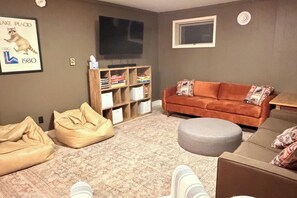 Ein Wohnzimmer mit einer Couch, einem Hocker, einem Sitzsack und einem Bücherregal.