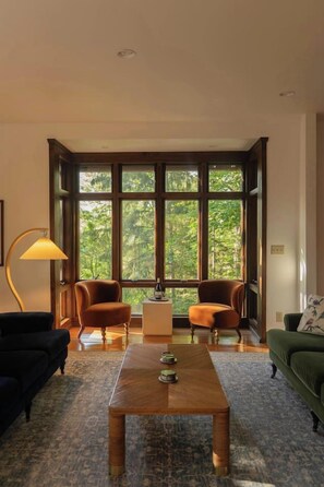 Ein Zimmer mit großem Fenster, zwei Sessel, einem Couchtisch, einer Stehlampe und einem grünen Sofa.