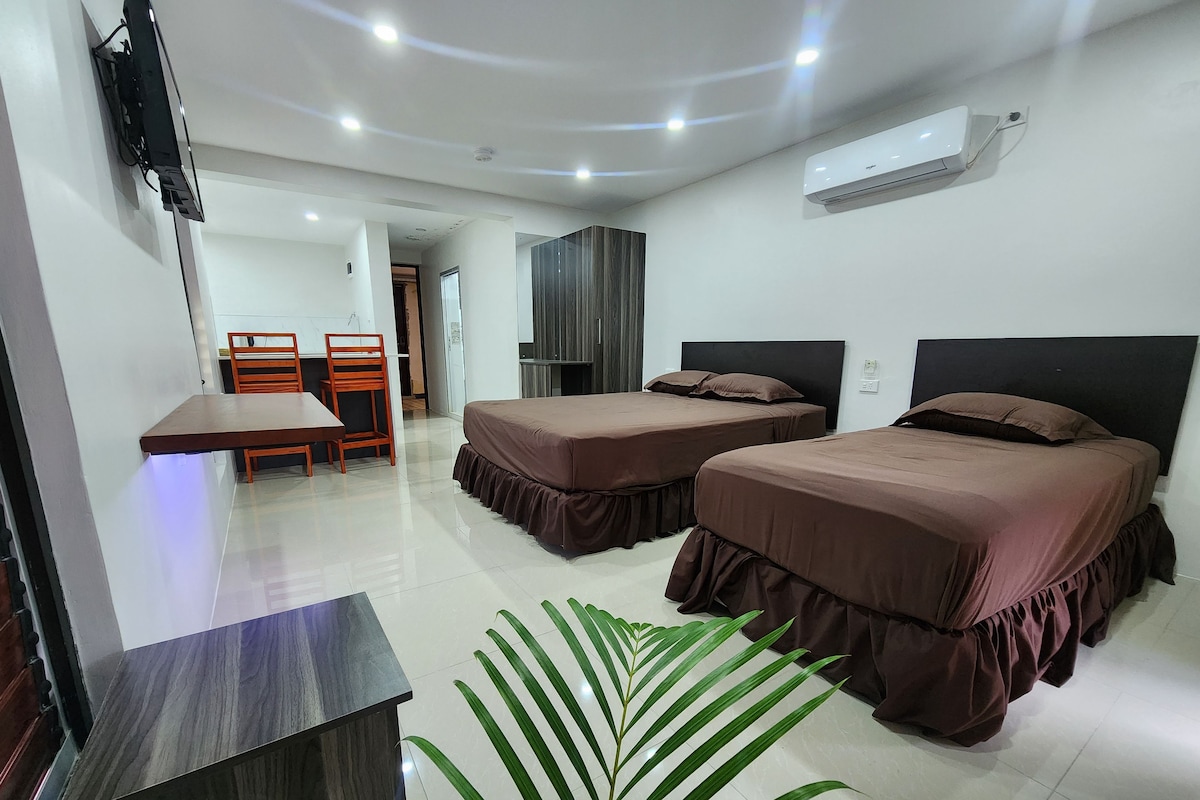 A hotel room with two beds, a desk, a chair, a TV, and an air conditioning unit.