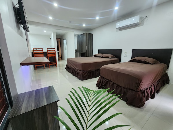 A hotel room with two beds, a desk, a chair, a TV, and an air conditioning unit.