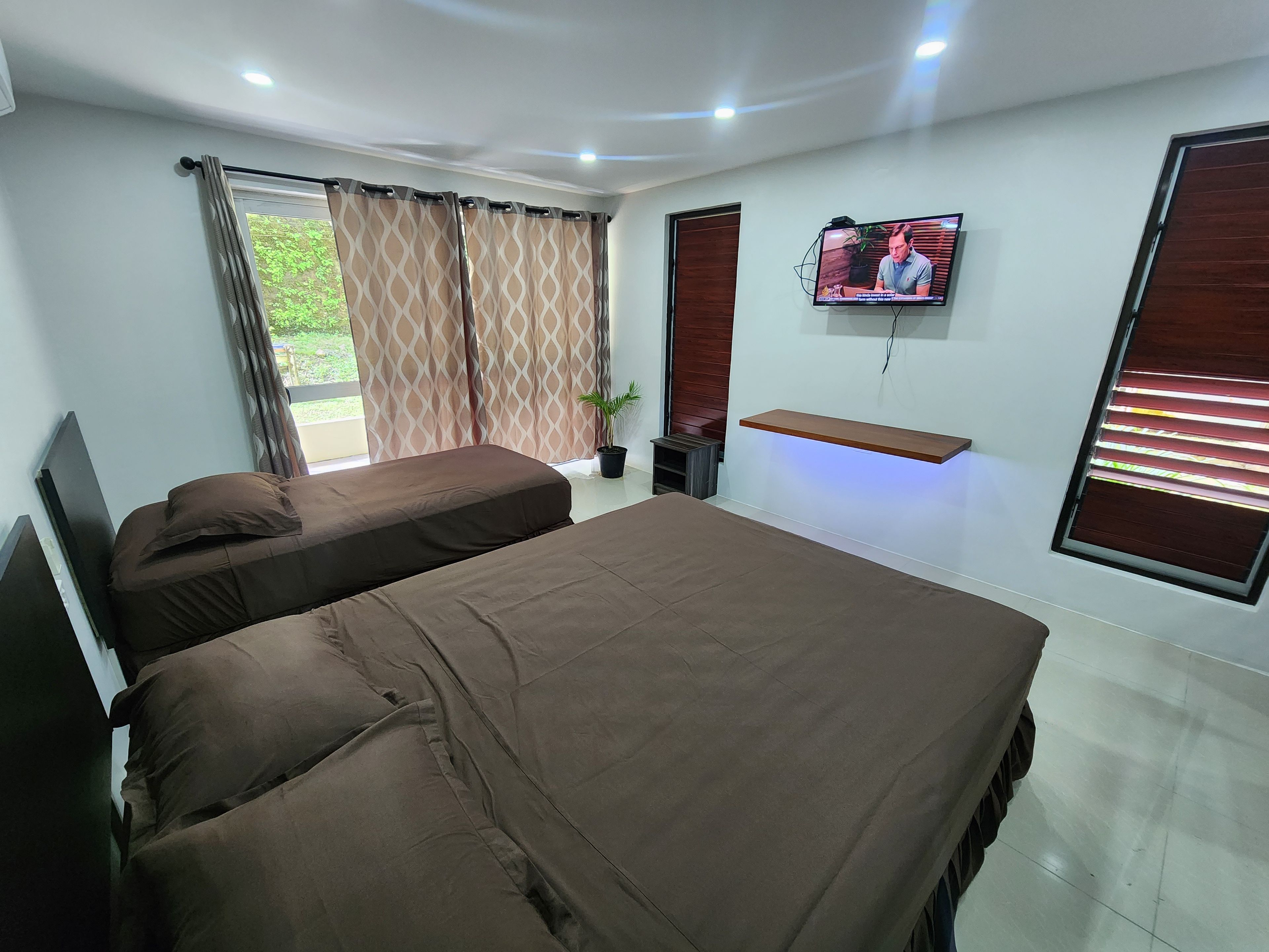 A hotel room with two beds, a television, a potted plant, and a window with curtains.