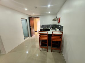 A compact kitchen with a dining area, featuring a small island, two wooden chairs, and a built-in sink. - Tropic Towers Apartments Hotel (Suva)