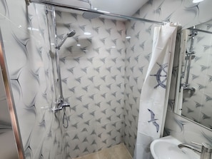 A bathroom with a glass-enclosed shower, a white sink, and a mirror with a ship wheel design. - Tropic Towers Apartments Hotel (Suva)