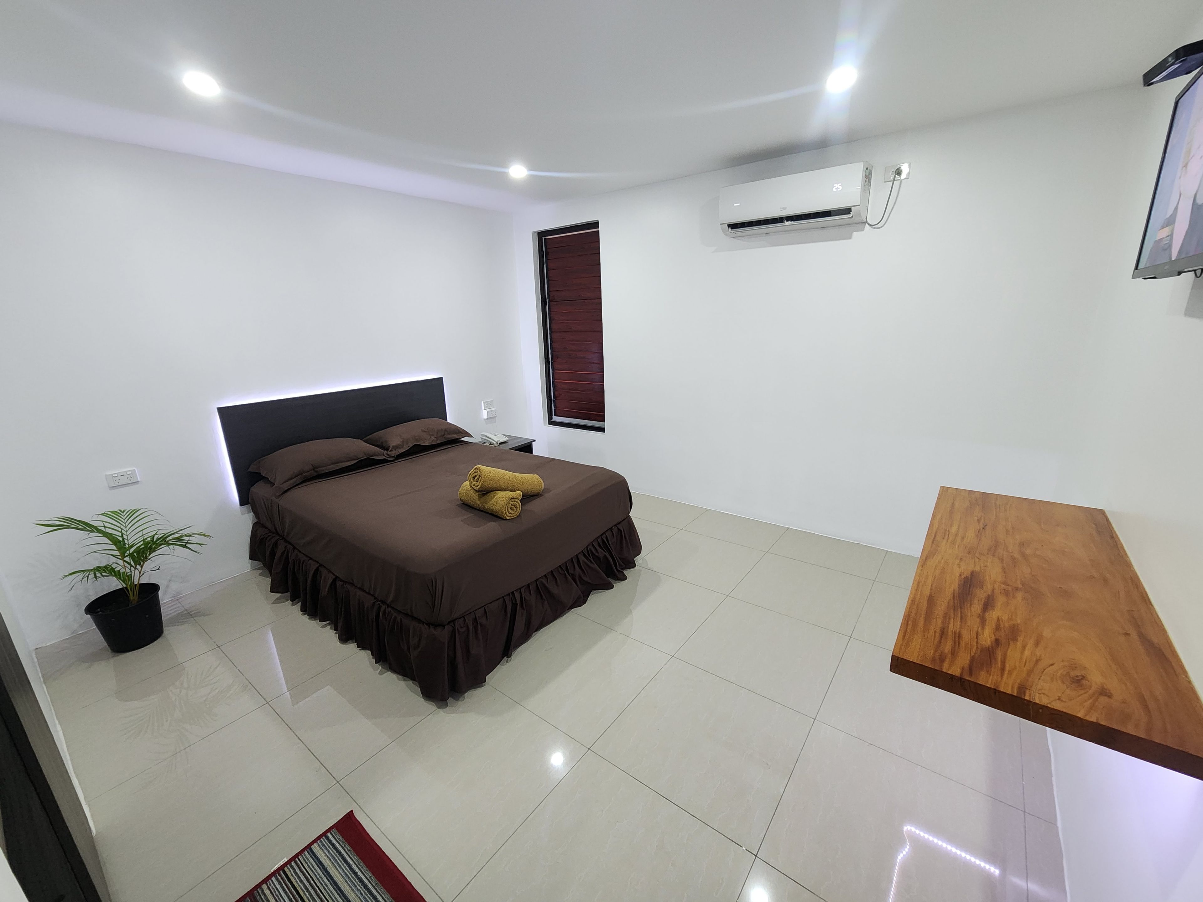 Un dormitorio moderno con una cama grande, una mesita de noche, una planta en maceta y un equipo de aire acondicionado.