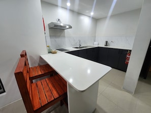 A modern kitchen with a white countertop, dark cabinets, and a wooden bench. - Tropic Towers Apartments Hotel (Suva)