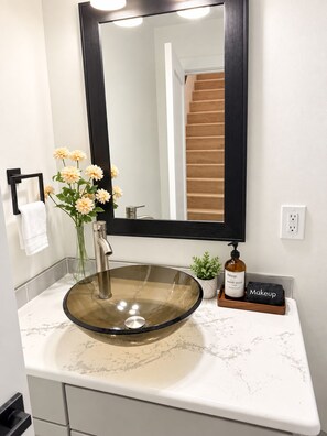 A bathroom with a vessel sink, a mirror, a towel rack, a vase with flowers, and a makeup station. - Spacious 5BR Tacoma Home - Sleeps 9 - Hilltop -Fenced Yard + Playroom (Tacoma)
