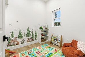 Ett lekrum för barn med en väggmålning som föreställer en skog, en matta med alfabetet och en bokhylla.