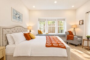 A bedroom with a large bed, two bedside lamps, a window with blinds, a chair, and a small table with a lamp. - Spacious 5BR Tacoma Home - Sleeps 9 - Hilltop -Fenced Yard + Playroom (Tacoma)