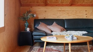 A cozy room with a black leather sofa, a small wooden side table, a round wooden coffee table, and a patterned rug. - Reverie Barn | Sauna + Ocean & Nature (Apollo Bay)