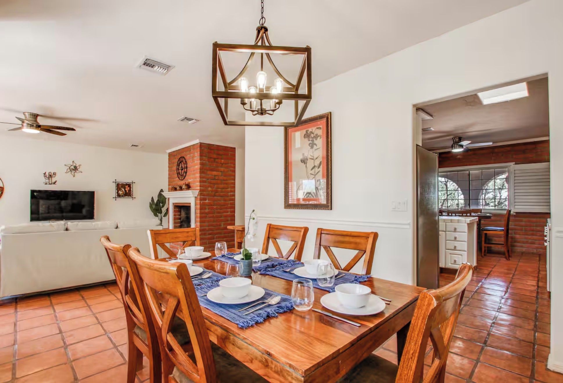 A dining area with a wooden table set for four, a brick fireplace, and a ceiling fan.
