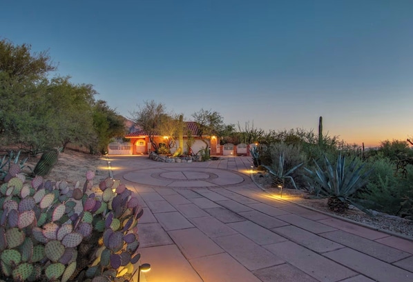 A paved pathway leading to a building with a red-tiled roof, surrounded by desert vegetation.