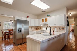 A modern kitchen with white cabinetry, a stainless steel refrigerator, a built-in stove, and a large island with a sink.