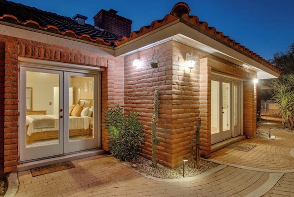 Una casa de dos pisos con fachada de ladrillo, puerta corrediza de vidrio como entrada y un pequeño patio con plantas.