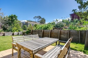 An outdoor patio with a wooden table and benches, surrounded by a wooden fence and greenery. - Summer In Blairgowrie (BLAIRGOWRIE)