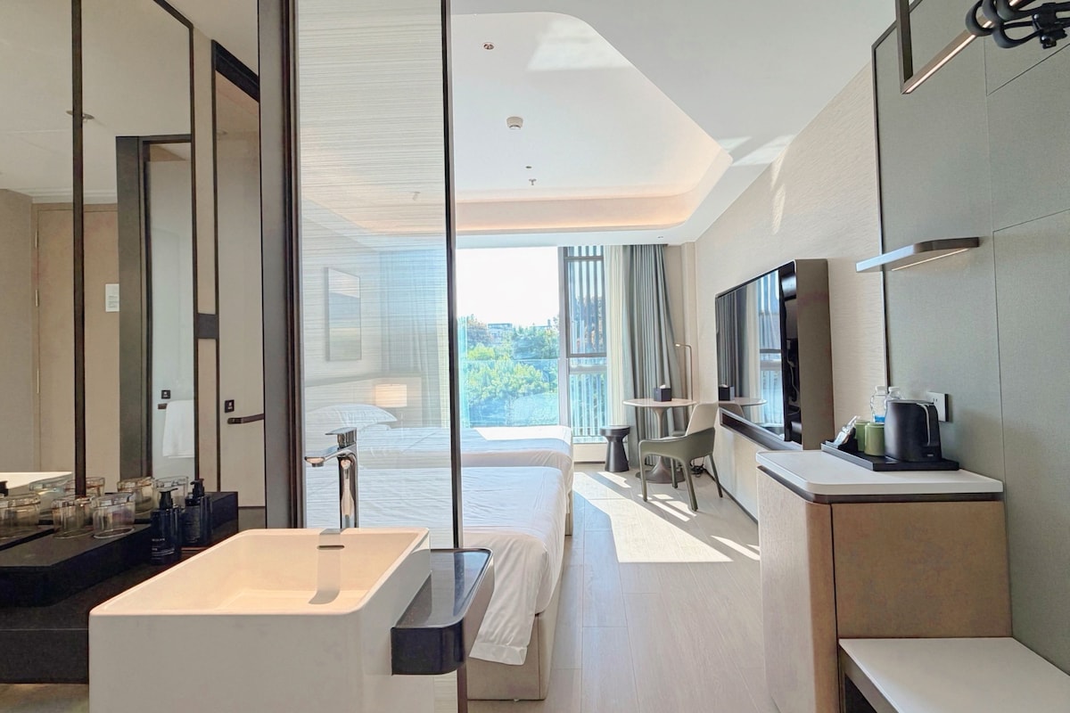 A modern hotel room with a large bathtub, a flat-screen TV, and a balcony with a view.