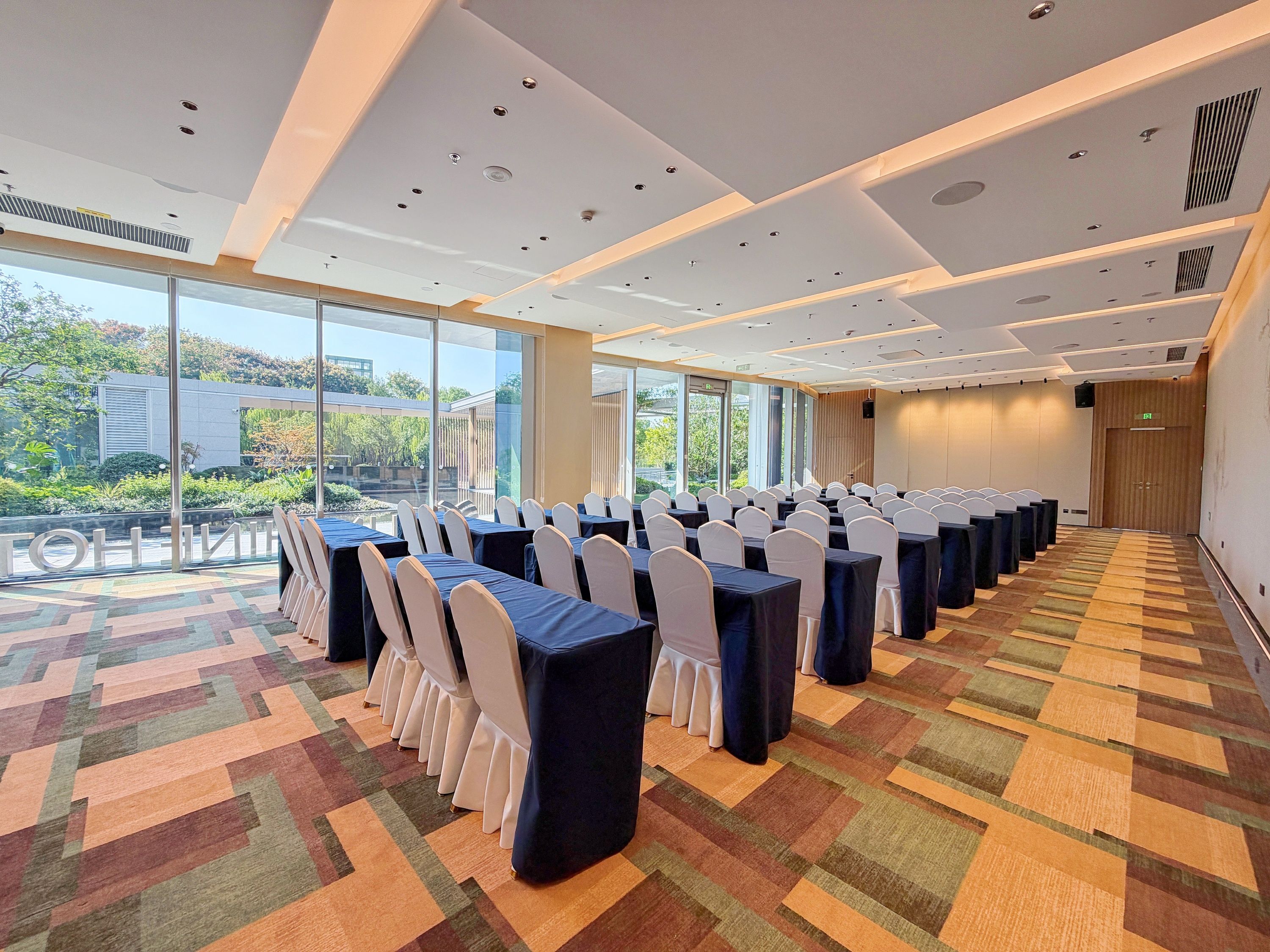 A conference room with rows of tables and chairs, large windows, and a patterned carpet.