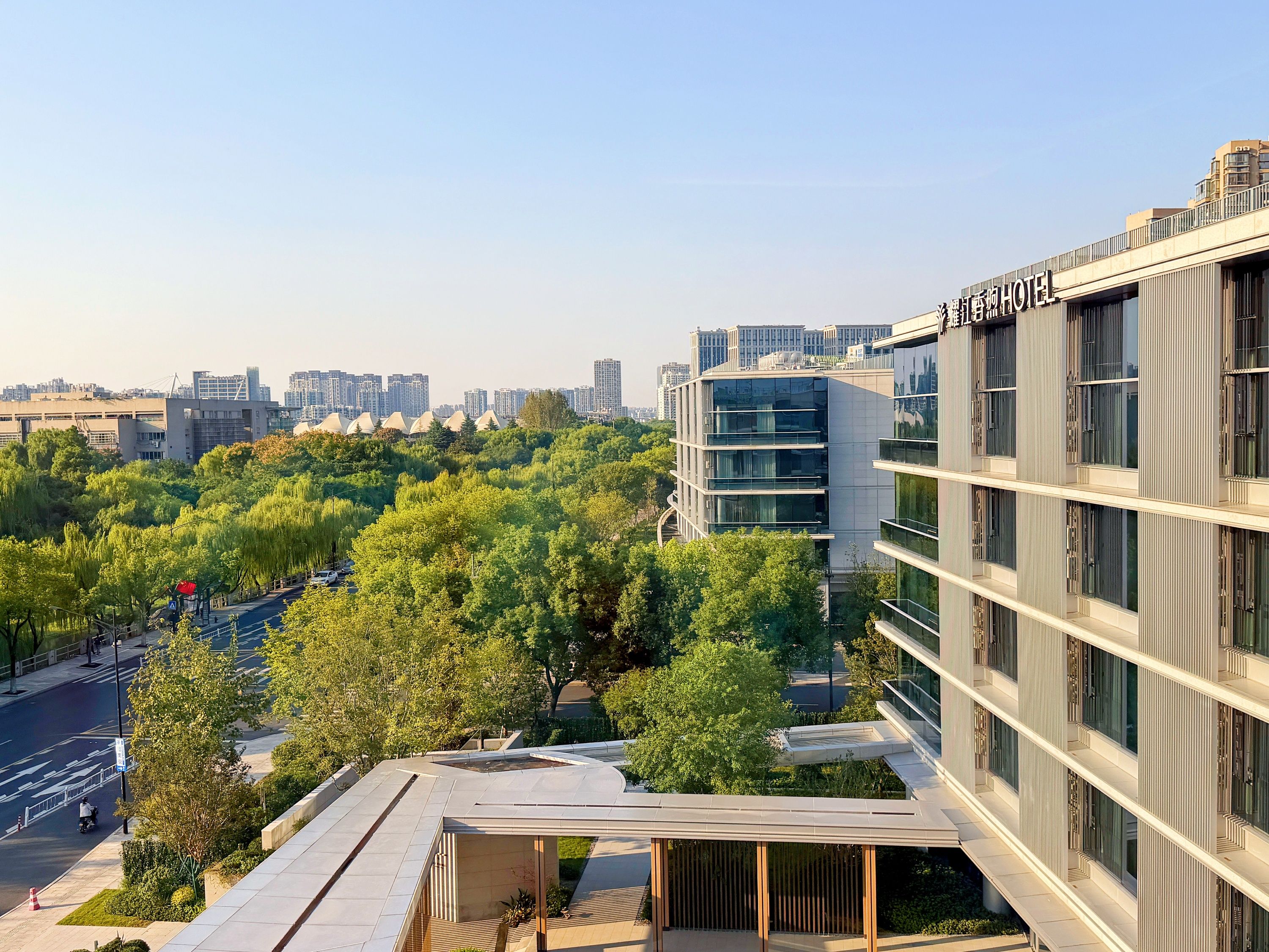 Un hotel moderno con terrazza panoramica, immerso nel verde e circondato da edifici urbani.