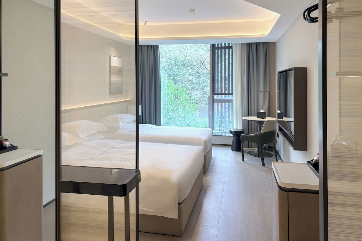 Una habitación de hotel moderna con cama, mesita de noche, escritorio, silla y un espejo grande.