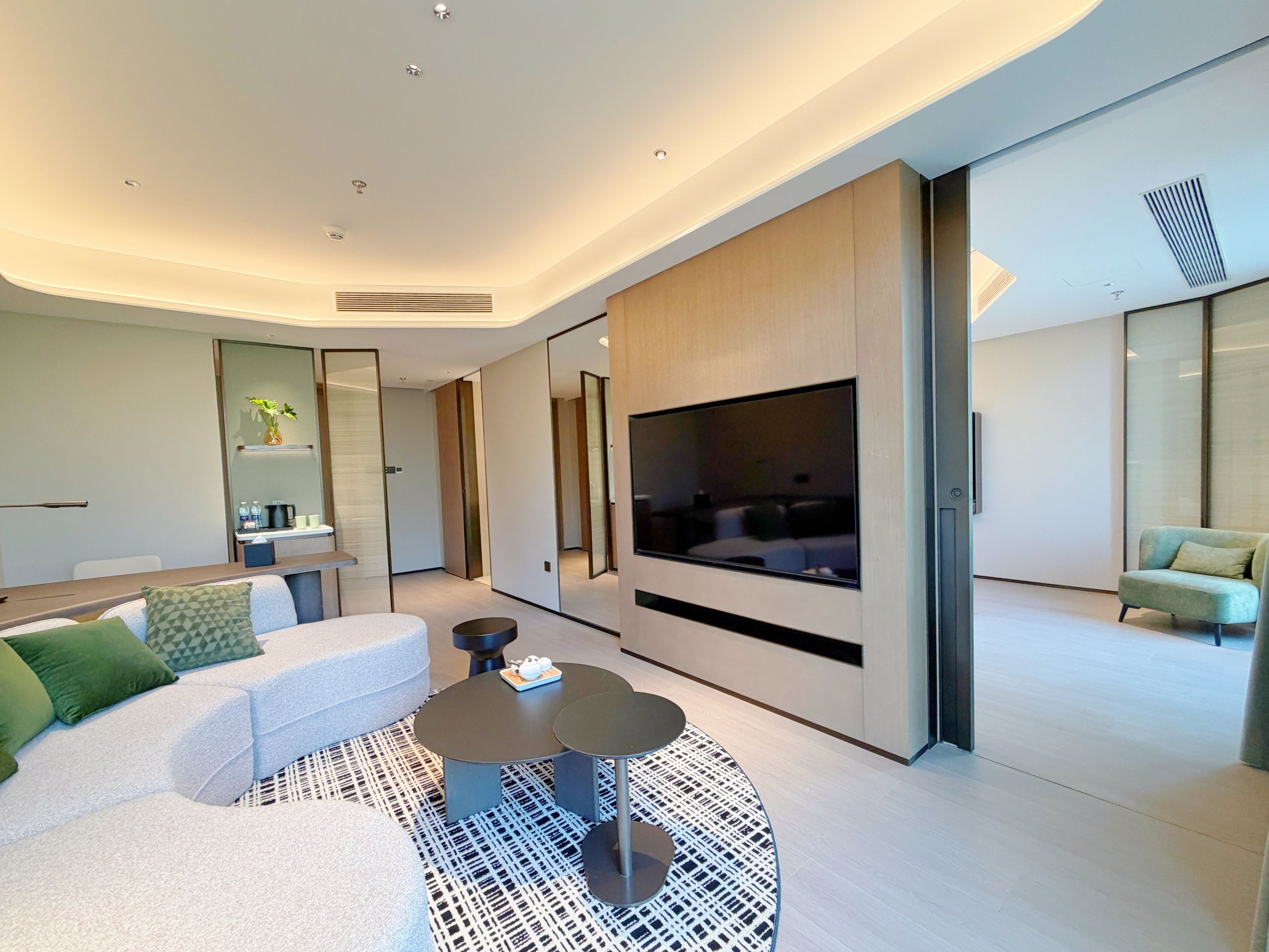 A modern living room with a sectional sofa, a round coffee table, and a flat-screen TV mounted on a wall.