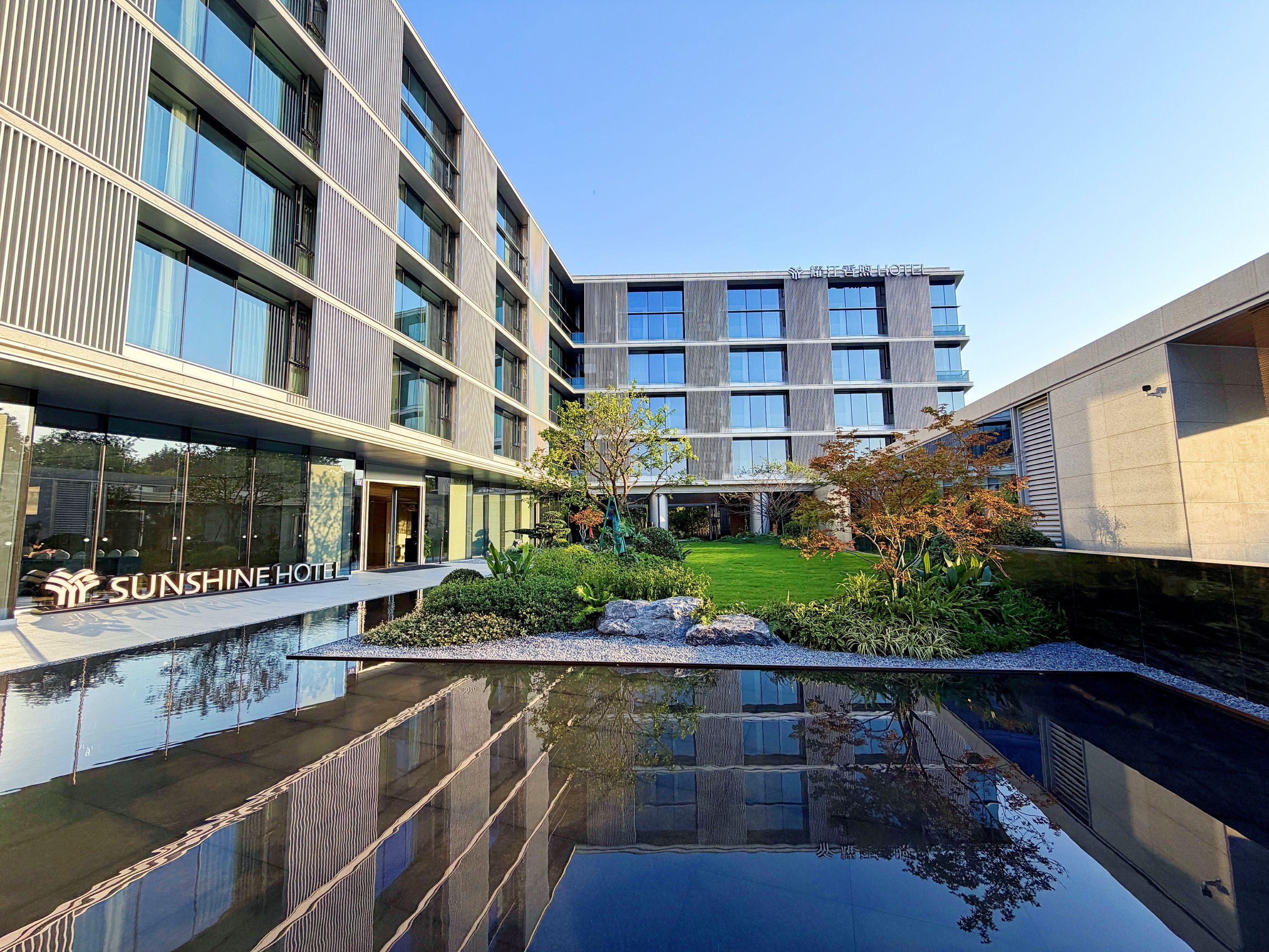 Un hotel moderno con una piscina a specchio, aree verdi e cielo sereno.
