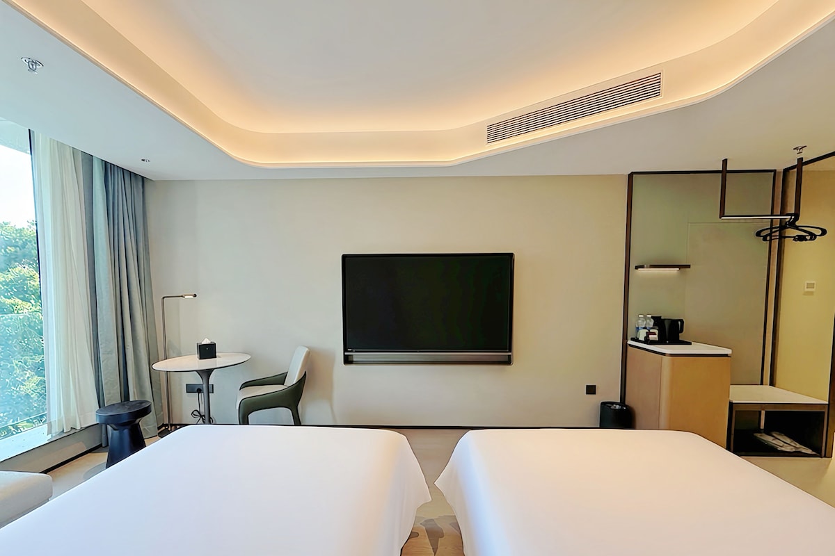 A hotel room with two beds, a desk, a chair, a TV, and a bathroom.
