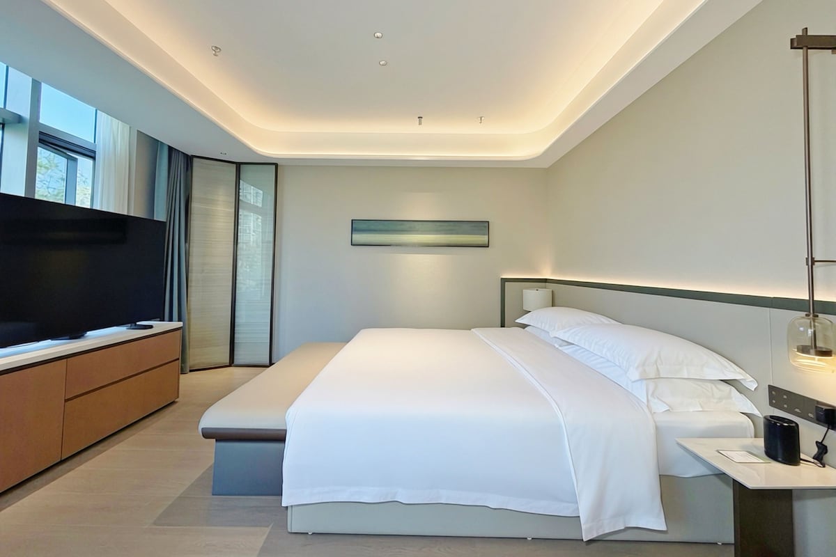 A modern hotel room with a large bed, a flat-screen TV, a bedside table, and a window with a view.