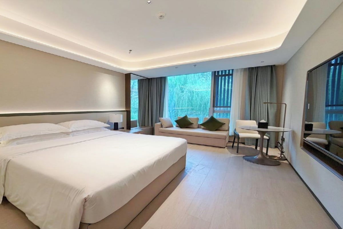 A modern hotel room with a large bed, a sofa, a small table, and a mirror.