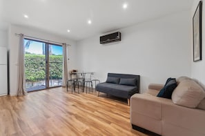 Una sala de estar moderna con un sofá, una mesa de comedor con sillas y un ventanal corredero que da a un área exterior.