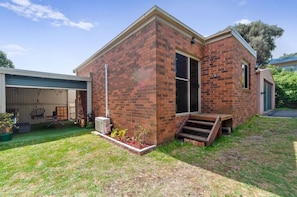 A two-story brick house with a covered patio, a small front yard with plants, and a visible garage door. - The Family Haven Sea Villas - Studio 1 & 2 (Rye)
