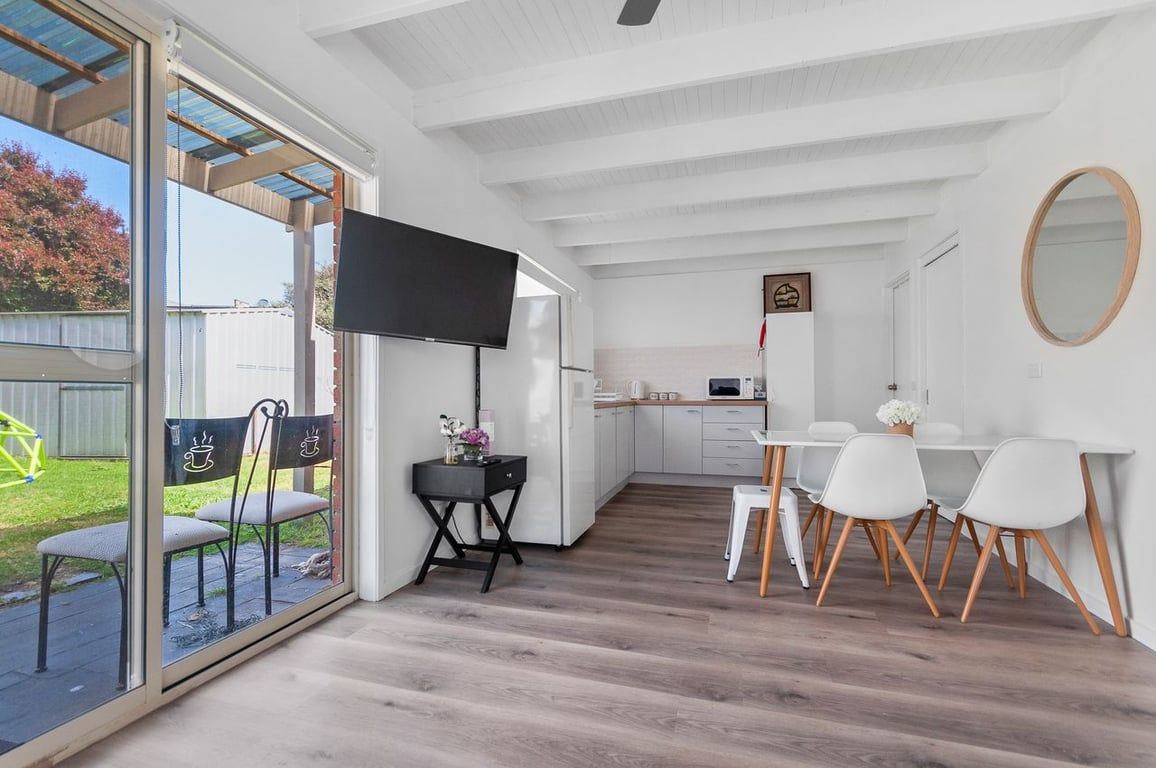 Une cuisine moderne avec des meubles blancs, un coin repas avec des chaises blanches et une grande fenêtre donnant sur un jardin.