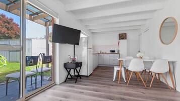 A modern kitchen with white cabinets, a dining area with white chairs, and a large window overlooking a garden.