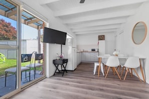 A modern kitchen with white cabinets, a dining area with white chairs, and a large window overlooking a garden. - The Family Haven Sea Villas - Studio 1 & 2 (Rye)