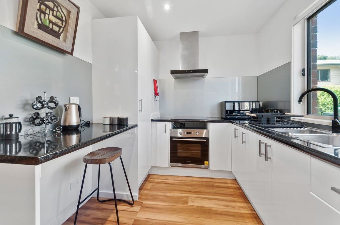 A modern kitchen with white cabinets, stainless steel appliances, and a wooden stool.
