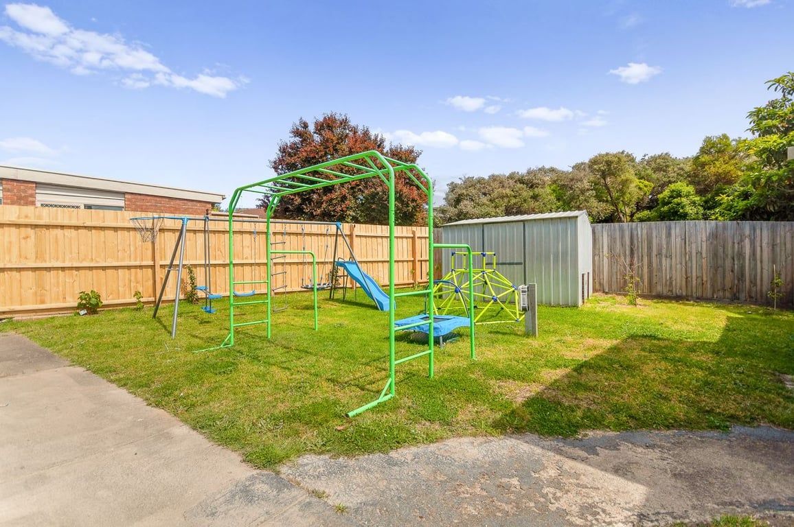 A backyard with a green play structure, a wooden fence, and a shed.