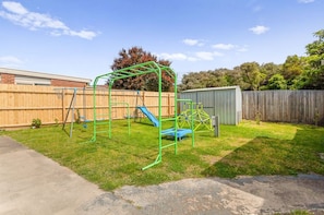 Un patio trasero con un parque infantil de color verde, una valla de madera y un cobertizo.